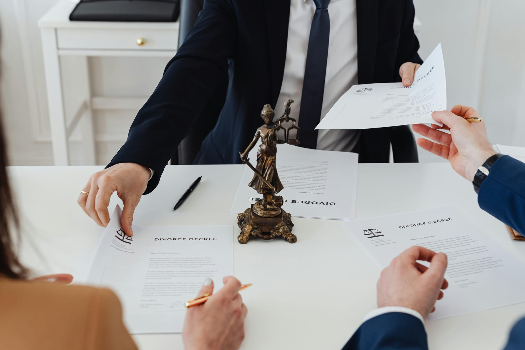 Personas revisando y firmando documentos legales sobre un escritorio, con una figura de la justicia al centro, representando procesos institucionales y toma de decisiones formales.