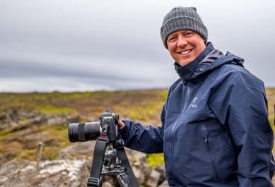 David Knoble in a rain coat with a Leica S on a tripod and an Iceland mossy background.