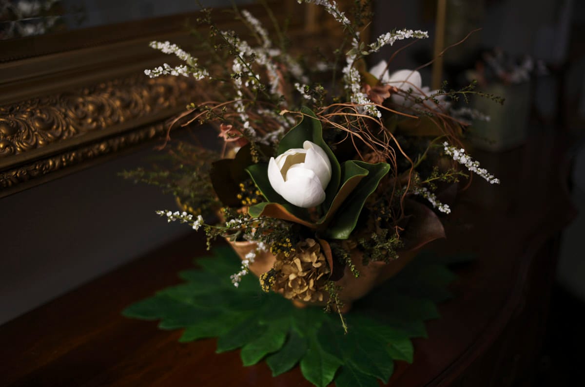 A darker image of the pottery vase with flowers sitting on a bureau
