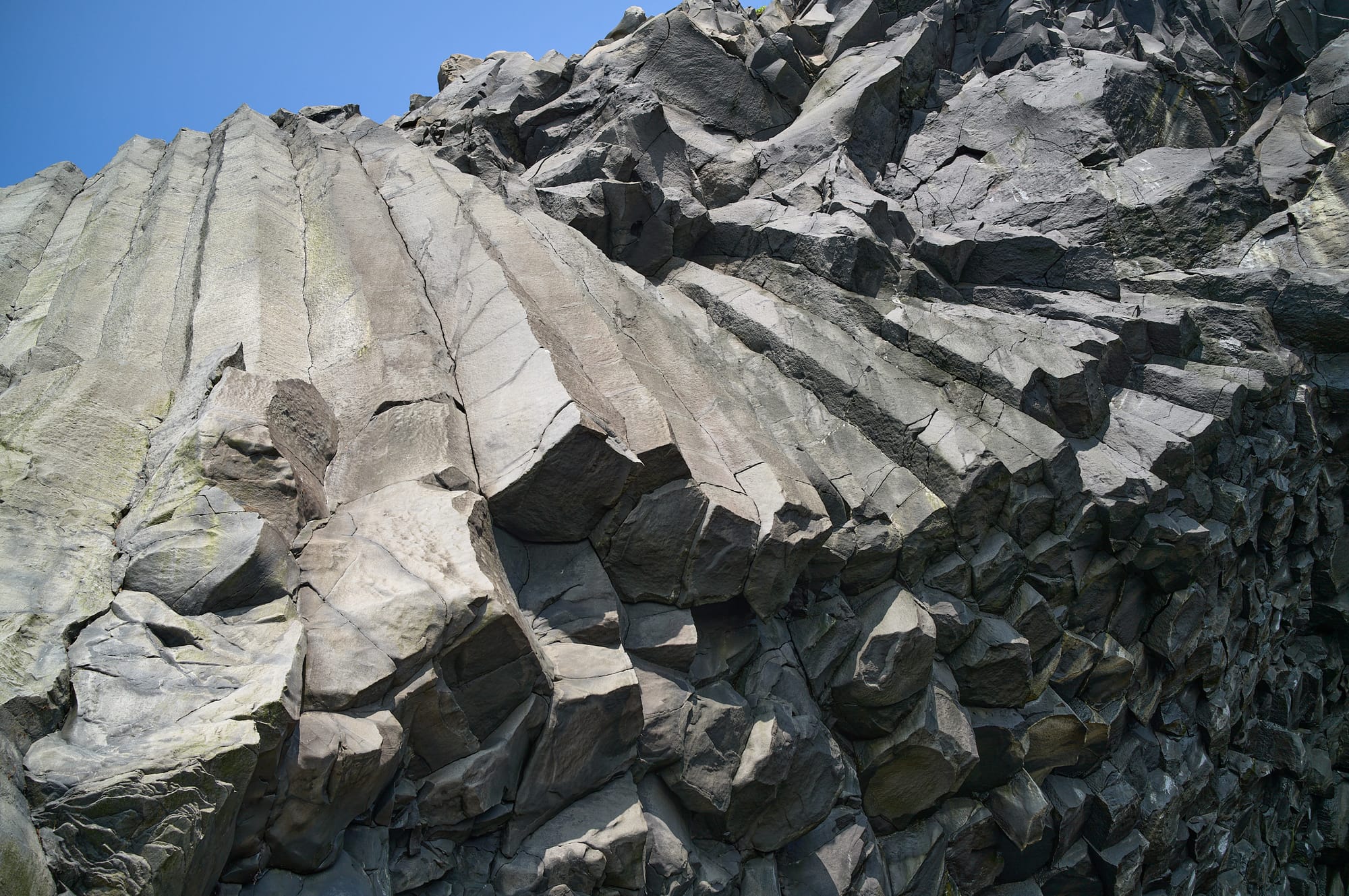 Vertical hexagonal rocks structure looking up at the blue sky.