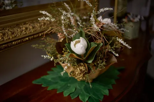 A pottery vase of flowers including a magnolia flower, sitting on a bureau