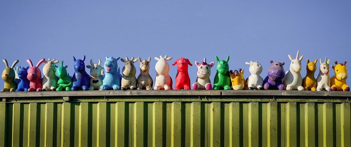 dozens of colorful stuff-animals lined up in a row on top of a moss green shipping container