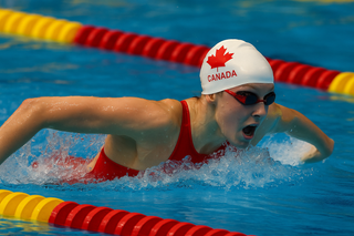Canadian competitive swimmer in red and white gear racing through a blue pool, representing Canada at the World Championships