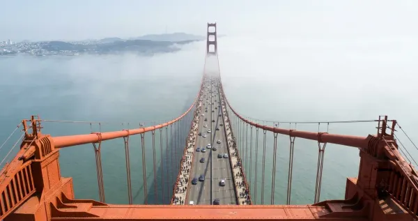 A view from atop the Golden Gate Bridge tower, looking down at people walking across the bridge and cars traveling in the distance.