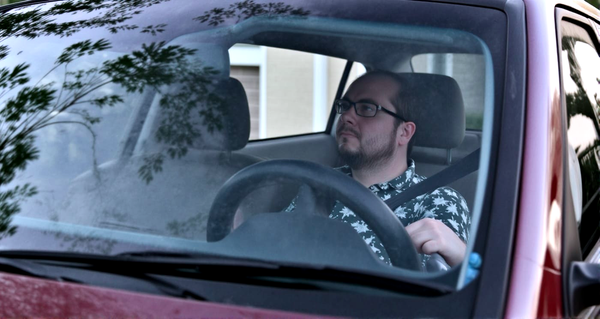 Man sitting in driver's seat of vehicle looking into the rearview mirror.
