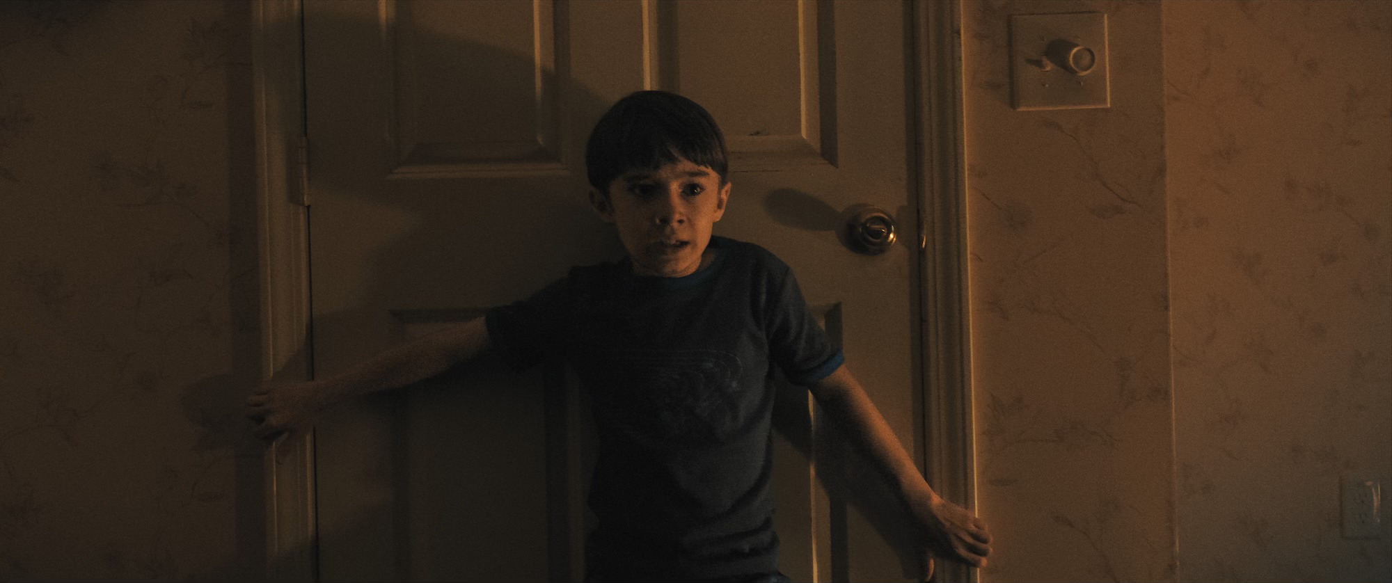 Alex (Cary Christopher) tries to keep a door barricaded in Weapons.