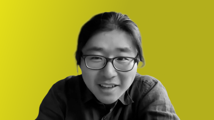 Leon Xiao leans on his desk while smiling.