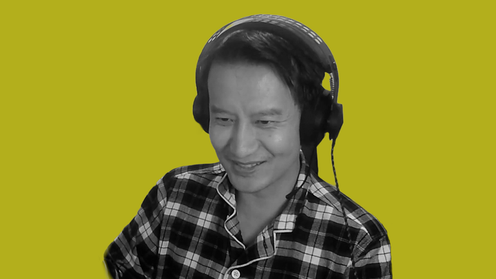 Minh "Gooseman" Le, in black and white, smiling at his PC screen in front of a background of grokludo yellow.