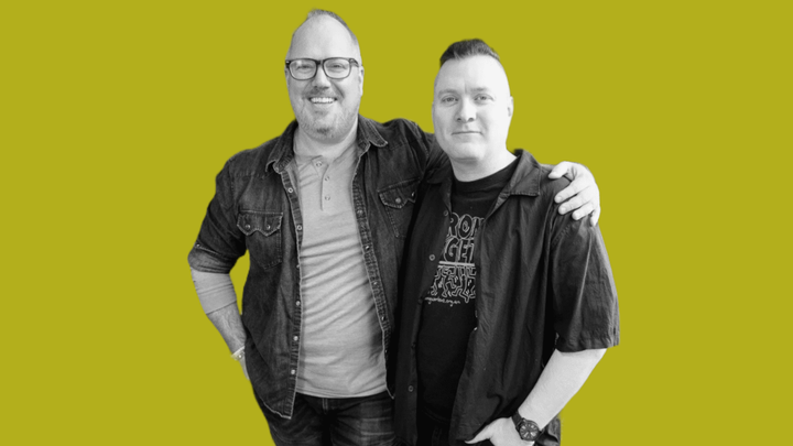 Guy Blomberg with his arm around Shay P Leighton's shoulder, smiling at the camera. The two are in black and white, in front of a background of grokludo yellow.