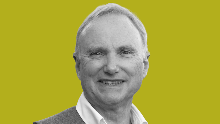 Tony Attwood, autism expert, smiles at the camera in black and white, in front of a grokludo yellow background.