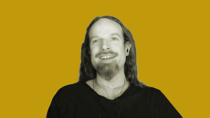 Ross Scott of the Stop Killing Games movement appears in black and white, smiling in front of an orange background, while talking on the grokludo podcast. 