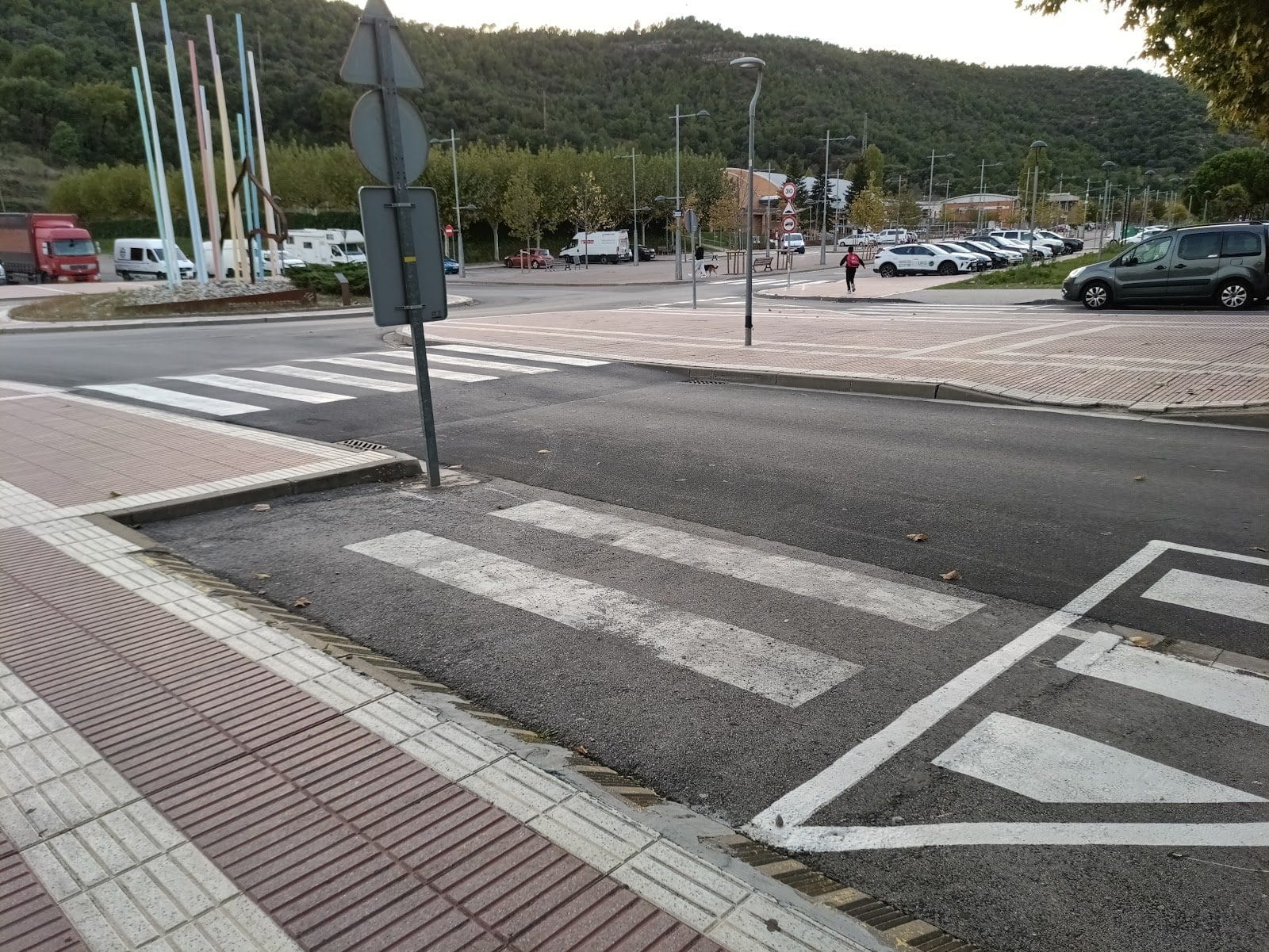 Paso de peatones cuyas bandas blancas quedan cortadas por un parche de asfalto nuevo, junto a una acera con pavimento podotáctil