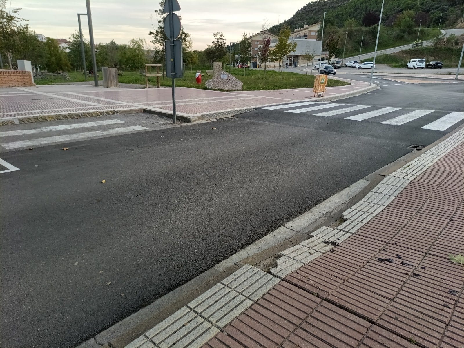 Vista general del cruce con asfalto recién extendido y las bandas del paso de peatones visibles solo en un lado