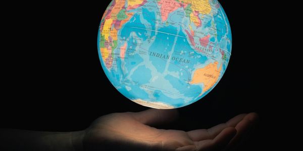 A glowing globe held above a pair of open hands against a dark background, turned toward the Indian Ocean.