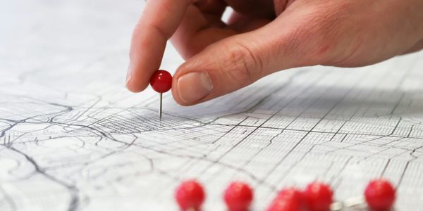 A hand pressing a red pin into a printed map.