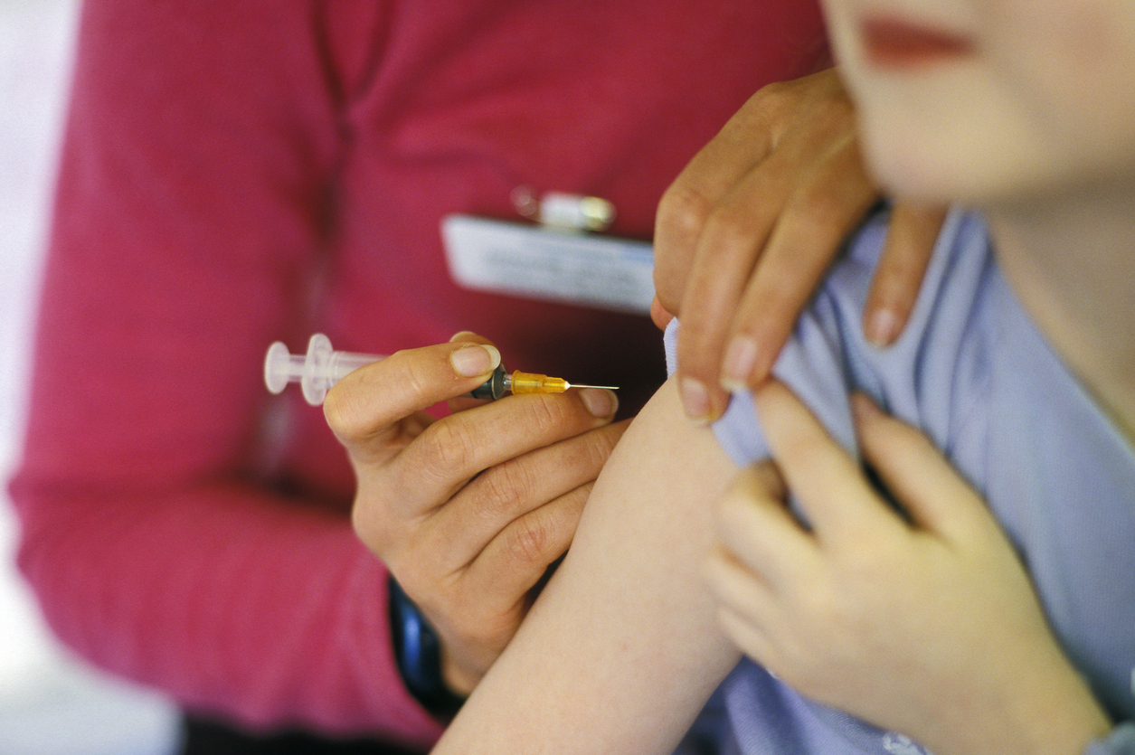 A child about to be given the MMR (mumps, measles, rubella) vaccination into their arm by a surgery nurse