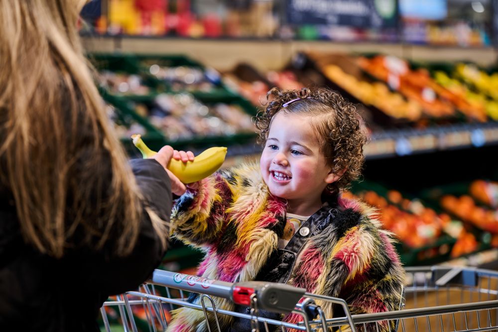 A young girl being given a banana by her mum in an Aldi supermarket