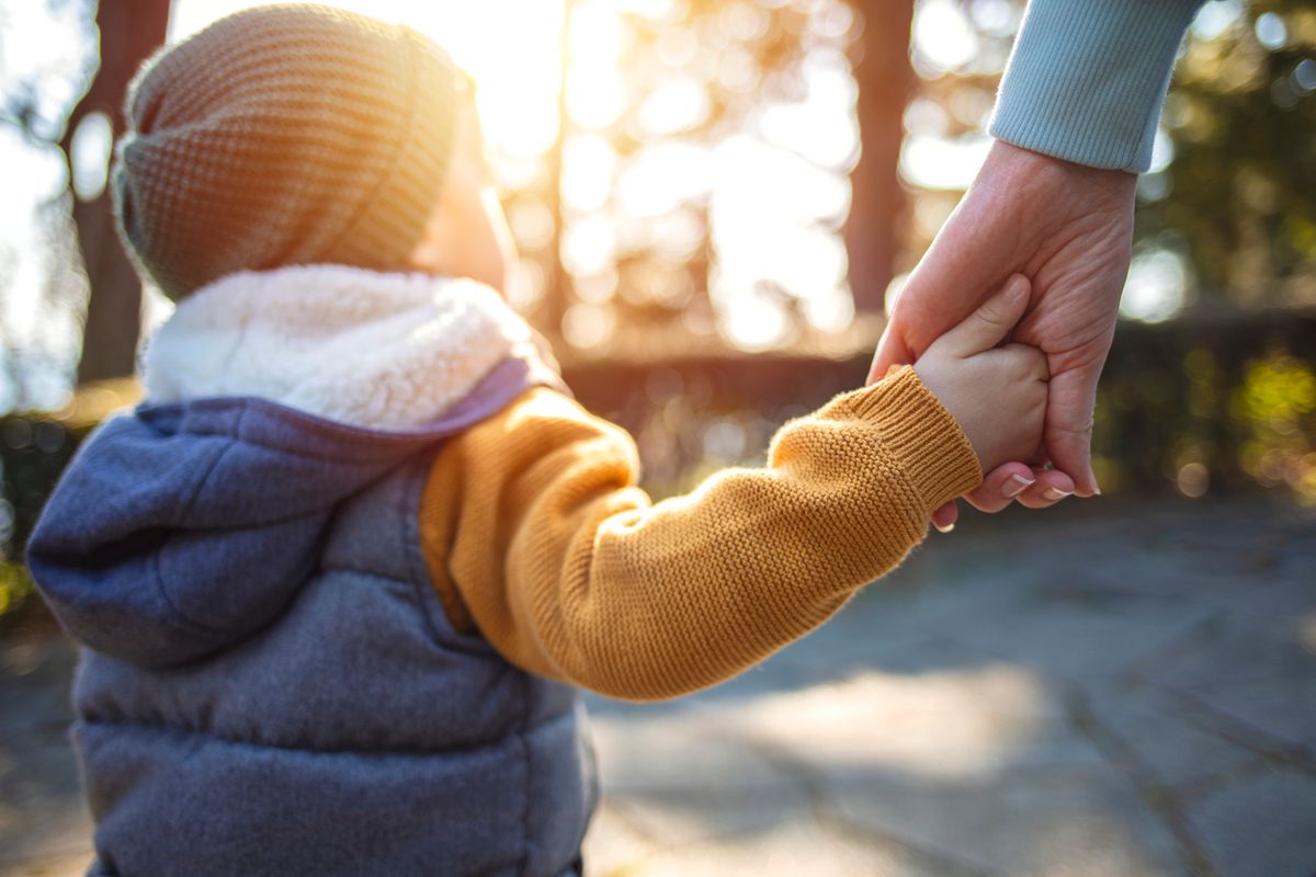 A young boy holding their parent's hand