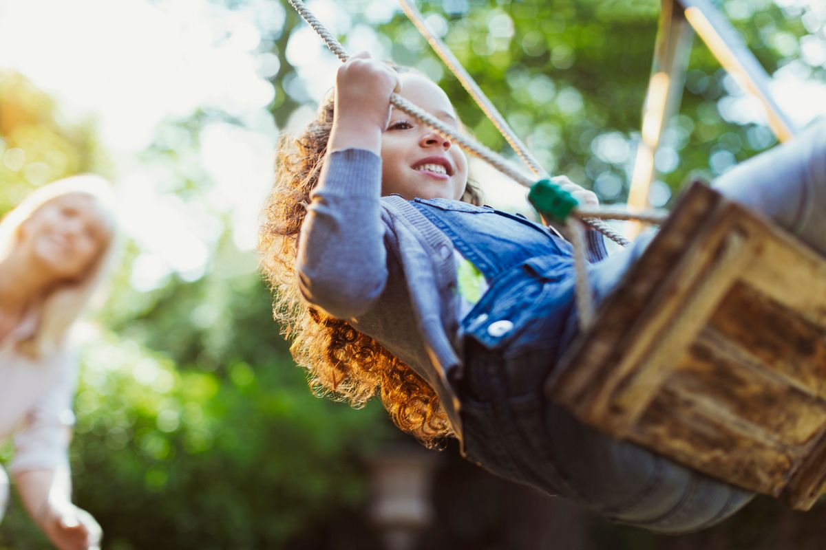 Mum pushing daughter on a swing in the summer