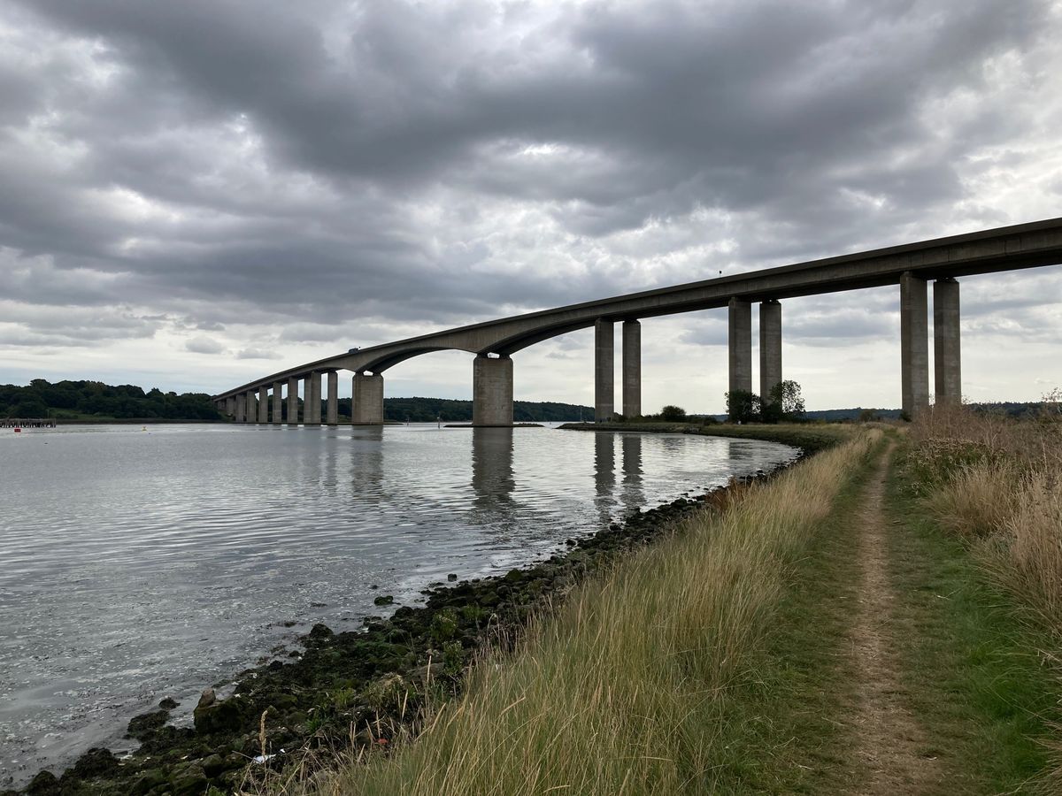View of the Orwell Bridge spanning the River Orwell with grassy riverbank in the foreground and cloudy sky above