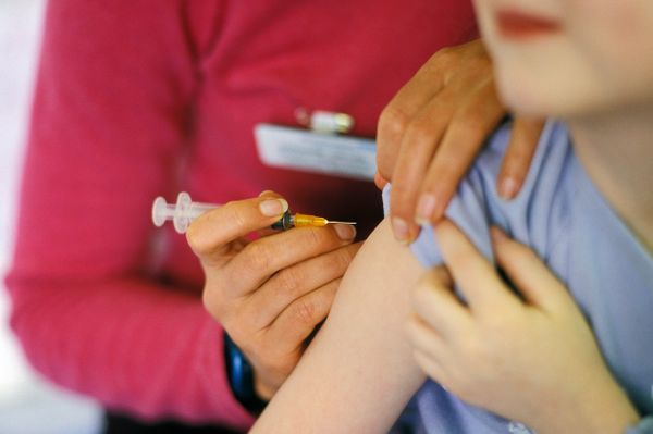 A child about to be given the MMR (mumps, measles, rubella) vaccination into their arm by a surgery nurse