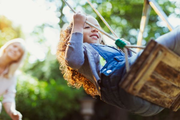 Mum pushing daughter on a swing in the summer