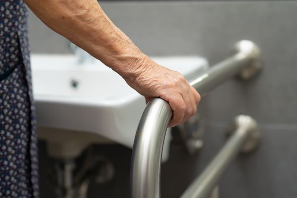 An elderly lady holding a support rail next to a sink