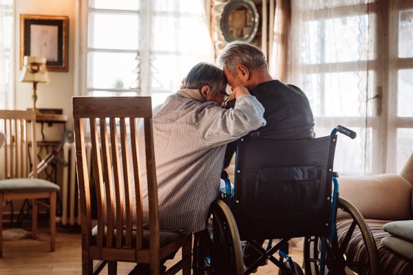 A woman siting on a chair next to her husband in a wheelchair