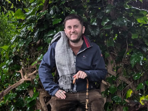 Daniel Lee Harvey, disability activist, seated in nature holding a walking stick