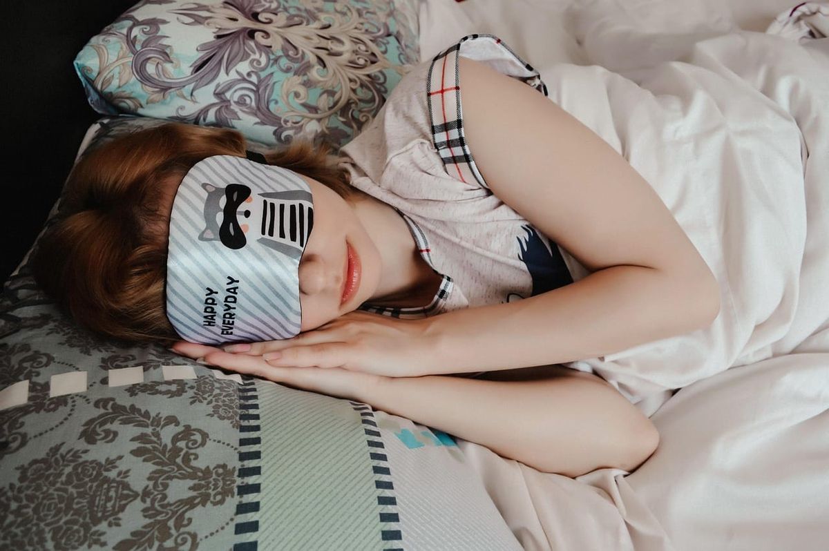 A person lying in bed, sleeping with a sleep mask in bed.