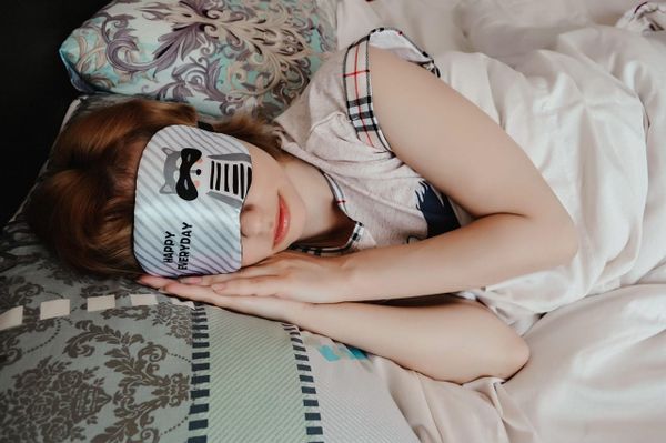 A person lying in bed, sleeping with a sleep mask in bed.