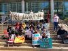 A group of Prakash Churaman's support sit with signs on the stairs of the Queens courthouse.