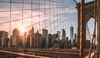 Close-up photo of the Brooklyn Bridge, the sun behind it.