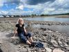 A woman in a black T-shirt and blue pants sits on the shore of the Ashokan Reservoir.