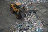 A yellow truck pushes a mound of recylables.