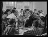 A black and white photograph of a large family siting around multiple tables eating thanksgiving dinner in 1940.