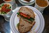 A vegan sandwich called The Gunther sits on a plate surrounded by various soups.