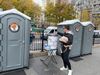 A man places a dollar bill into a trash can-turned-tip jar before using one of the port-a-potties at the base of the Brooklyn