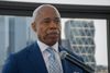 NYC Mayor Eric Adams, wearing a blue suit and a patterned tie, stands before a microphone.
