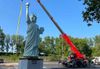 The Statue of Liberty replica being moved by crane in the Brooklyn Museum parking lot.