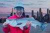 The author in a red rain jacket and blue denim baseball cap, holding a large striped bass in her hands, superimposed over a p