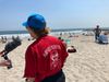 Rockaways lifeguard Janet Fash, in a red T-shirt and blue baseball cap, her back turned to the camera, at the beach.