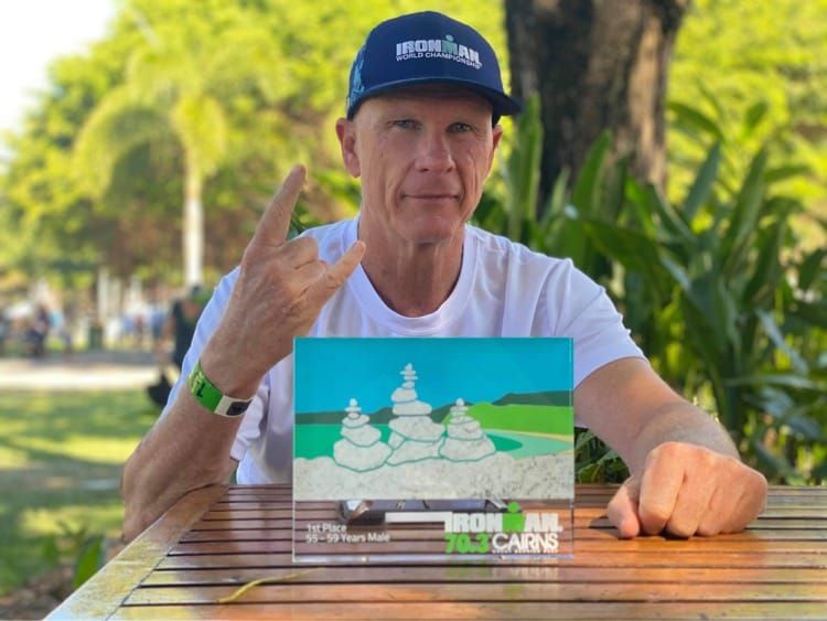 David Arnold in an Ironman cap with his 1st place 55-59 trophy from Ironman 70.3 Cairns