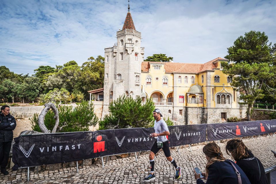 Runner passing a turreted yellow mansion on a barriered Ironman race course