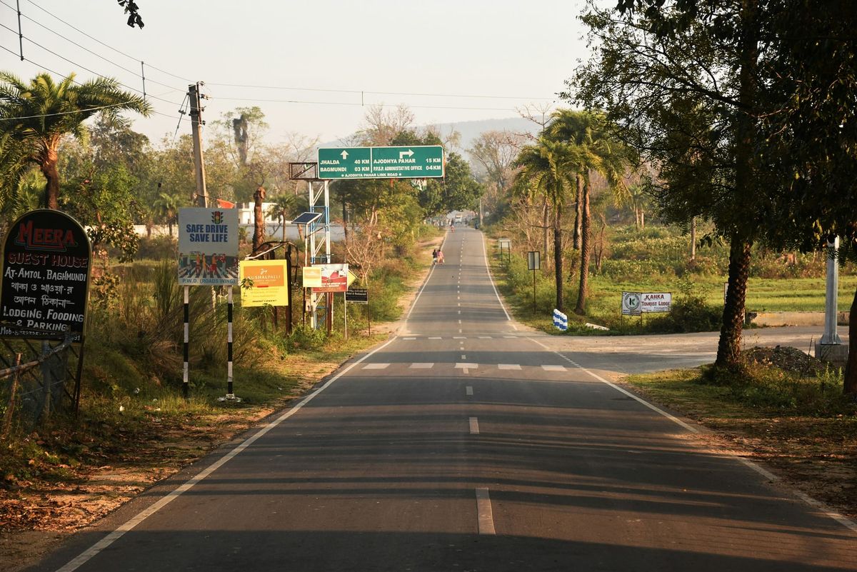 視角平視一條筆直延伸的柏油鄉間小路，兩旁是翠綠的草地與柔和的晨光，象徵著一條更輕鬆、明確的人生路徑。