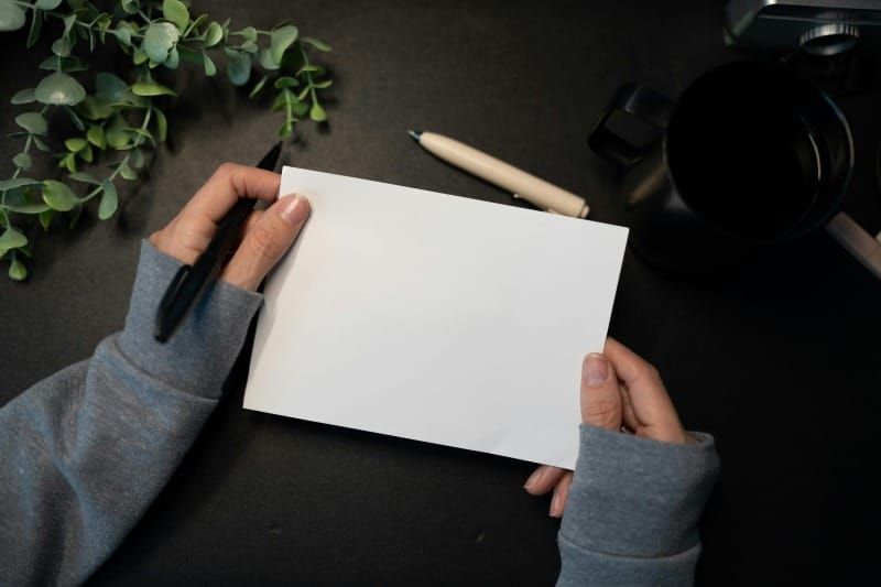 Hands holding a blank paper on a wooden desk, ready to write and release, symbolizing the start of healing.