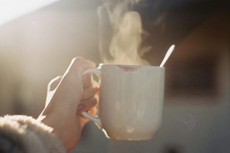 A hand holding a steaming cup toward sunlight, symbolizing human warmth and presence in the age of AI