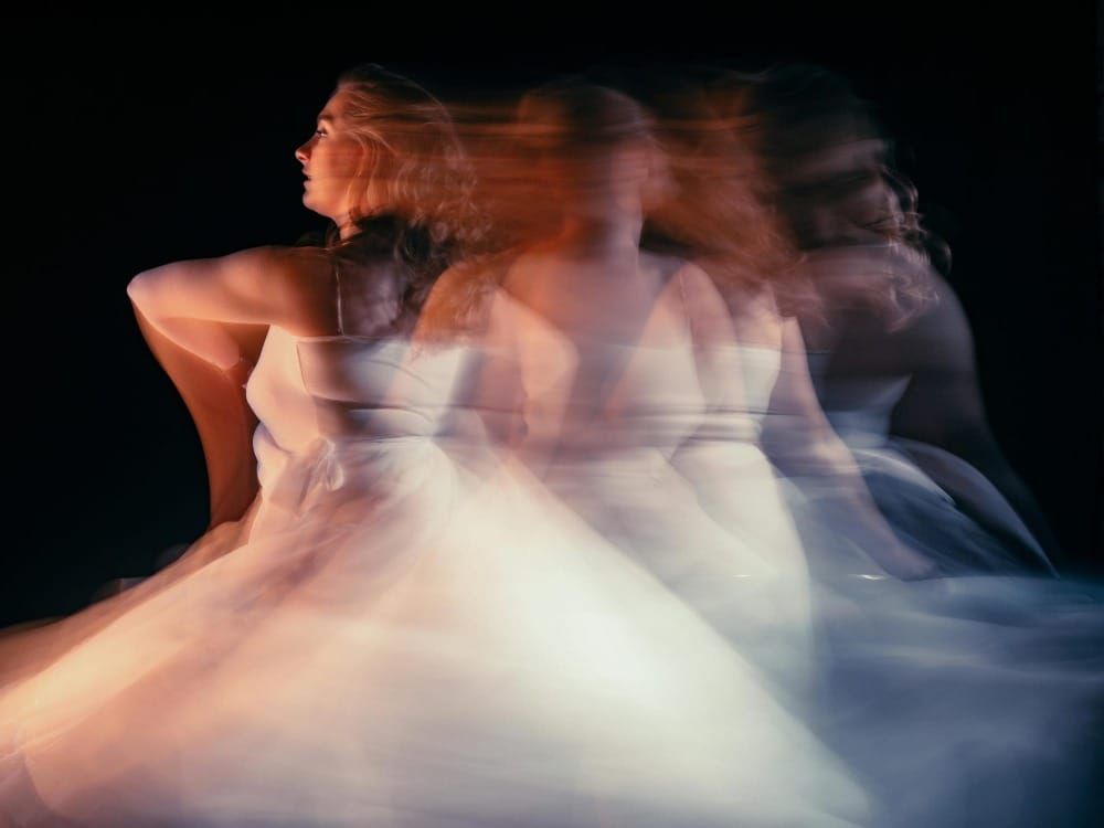 Long-exposure photo of a woman in white dress with motion blur creating multiple overlapping figures.