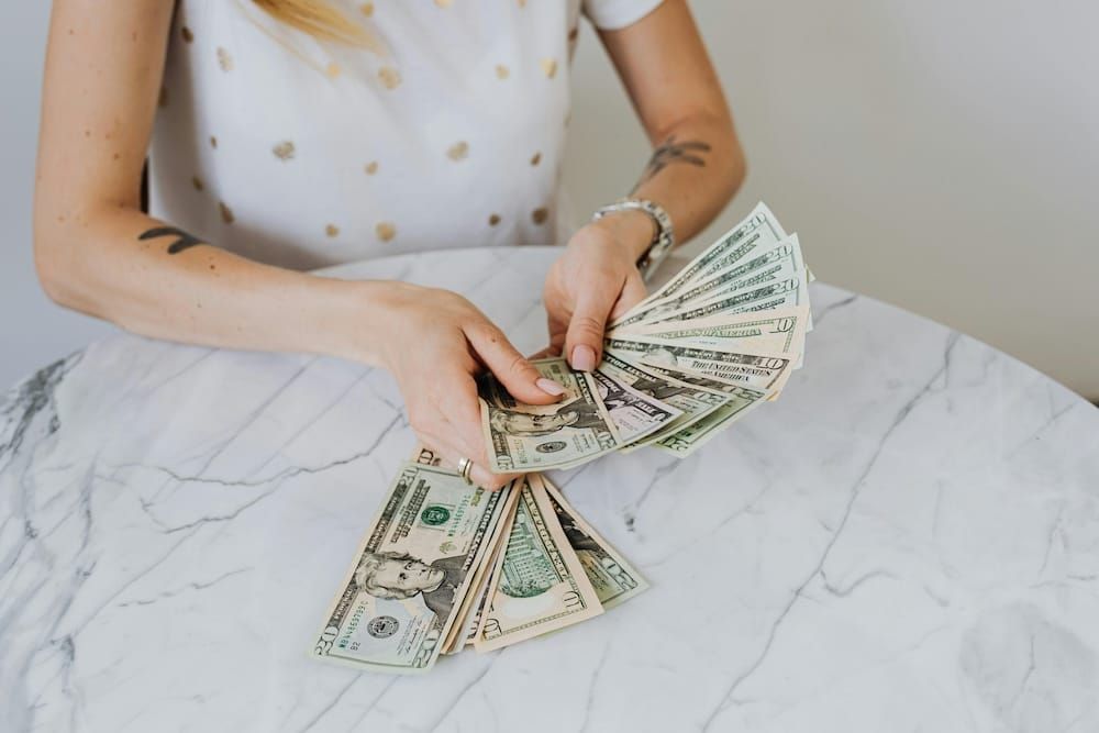 女性雙手展開多張美金鈔票，放在白色大理石桌上，象徵金錢流動與財務意識的覺醒