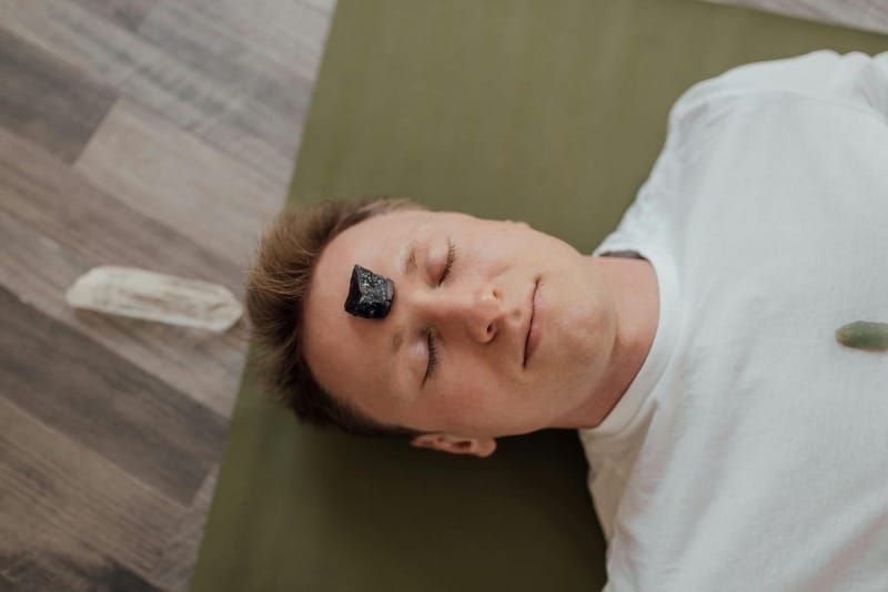 Person lying on yoga mat with healing crystal on forehead, emotional healing and mind-body connection